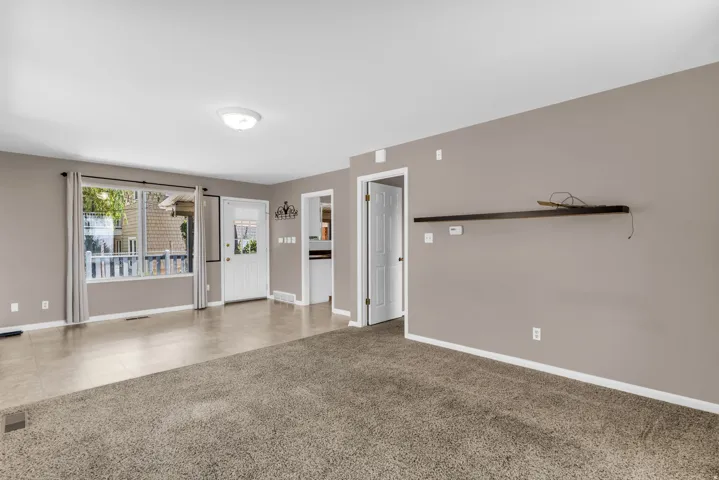 Spacious living area featuring neutral-toned walls, a large picture window, and a combination of carpet and tiled flooring