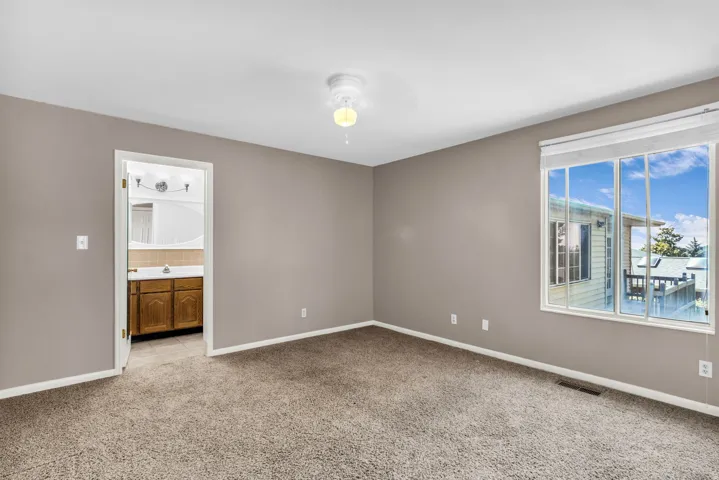 Spacious room with plush carpet flooring, a large window, and a ceiling fan
