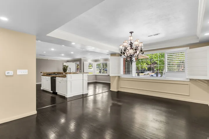 Dark wood-finish flooring with a white kitchen island, recessed lighting, and a decorative chandelier