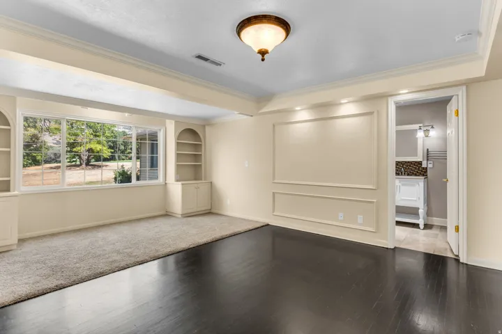 Hardwood-style flooring with a recessed carpet area, custom built-in shelving, large multi-pane windows, decorative wall molding, and crown molding