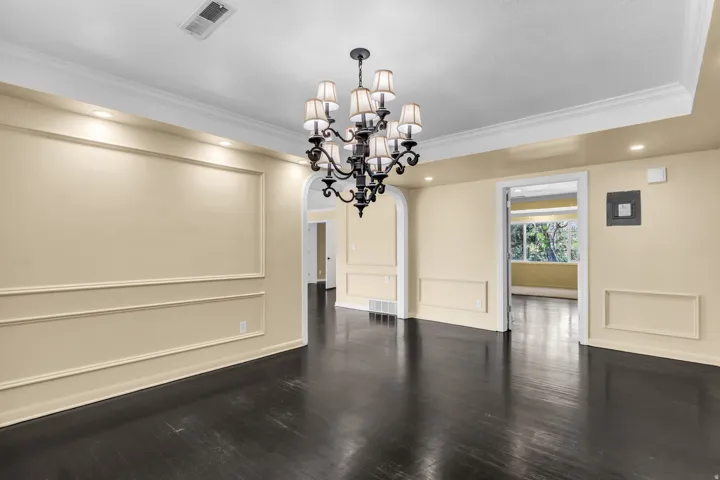 Dark wood-finish flooring with decorative wall molding, recessed lighting, and a multi-arm chandelier