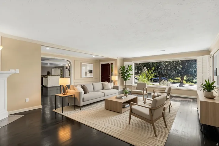 Expansive living area featuring a large picture window, dark wood-finish flooring, a white mantelpiece, crown molding, and an arched entryway to the kitchen