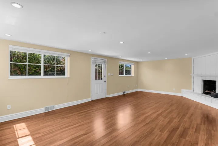 Wood-finish flooring, recessed lighting, white trim, white brick fireplace, and exterior access door
