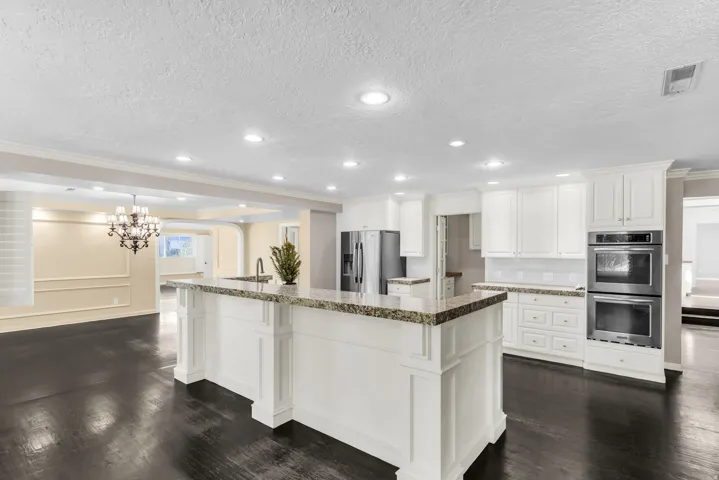 Kitchen featuring a large center island with a stone countertop, white shaker cabinetry, stainless steel double ovens, and recessed lighting