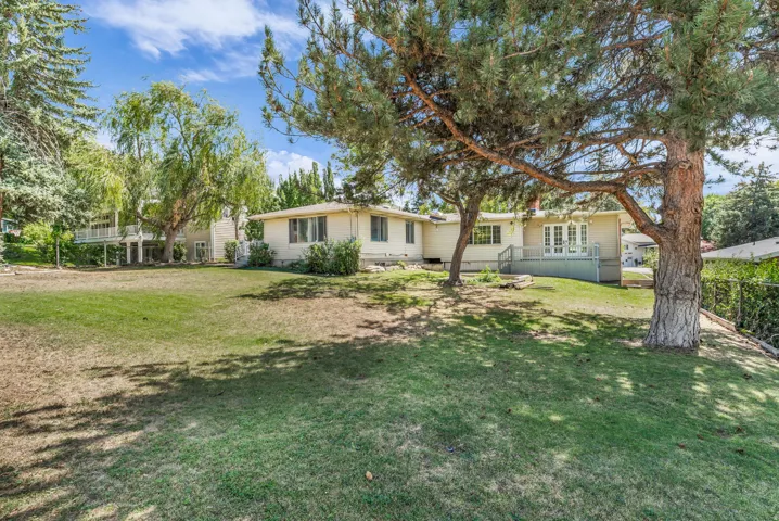 Expansive backyard with a manicured lawn, mature trees, and a raised deck with white railing