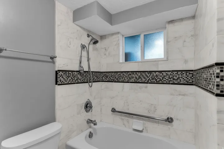 White tile surround with mosaic accent, built-in tub, and frosted window