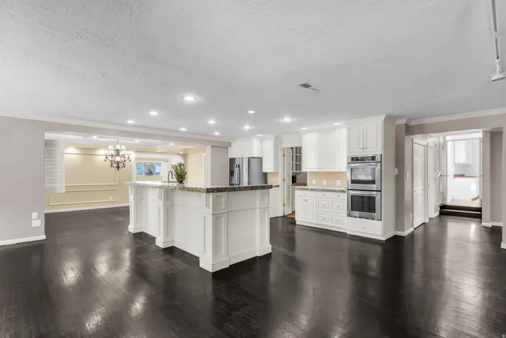 Spacious kitchen featuring white cabinetry, stone countertops, a large island with seating, dark wood-finish flooring, and built-in stainless steel double ovens
