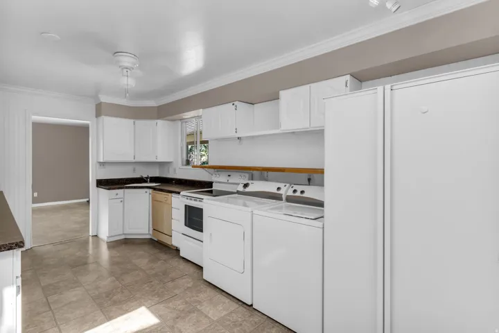 Full kitchen with white cabinetry, dark countertops, tiled flooring, and laundry appliances