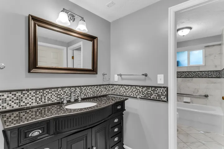 Vanity with integrated sink, mosaic tile backsplash, framed mirror, and chrome fixtures