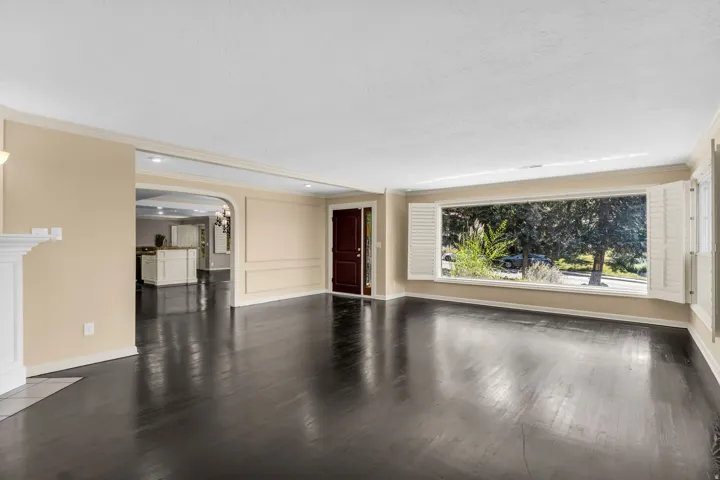 Dark wood-finish flooring, white fireplace mantel, arched doorway, and a large bay window with plantation shutters