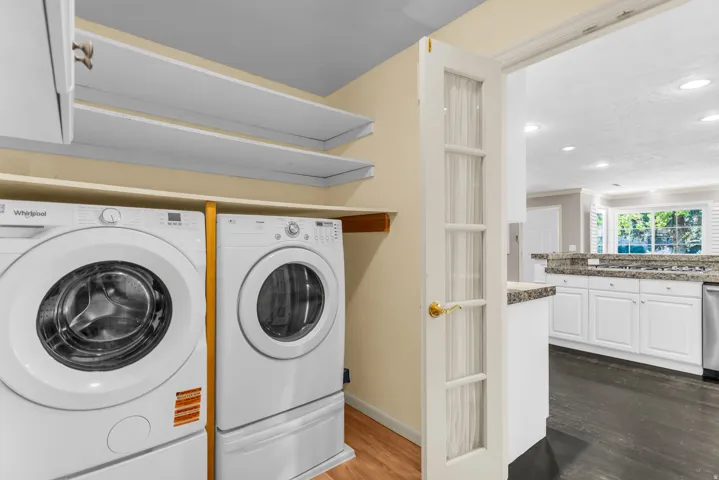 Laundry area with built-in shelving, glass-paned door, and wood-finish flooring