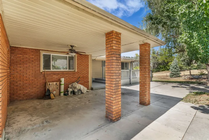 Covered carport with brick columns, an integrated ceiling fan, and concrete flooring
