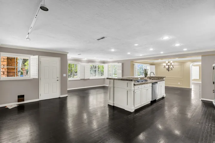 Spacious open-concept kitchen and great room featuring a large white cabinetry island with dark wood-finish countertops, stainless steel appliances, recessed ceiling lighting, and dark wood-finish flooring throughout