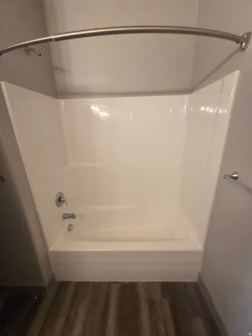White acrylic tub and shower combination with chrome fixtures and a curved shower rod