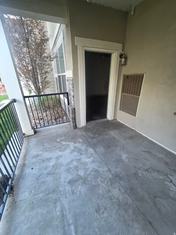 Covered outdoor patio with a concrete surface, black metal railing, and an exterior wall light fixture