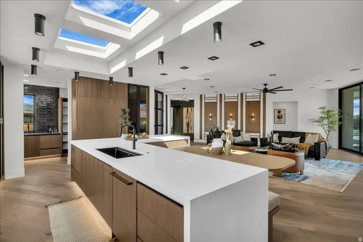 Open-concept kitchen and living area featuring multiple skylights, recessed lighting, wood-finish flooring, a kitchen island with a dark basin sink, and a multi-panel sliding glass door