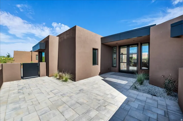 Contemporary stucco exterior with a flat roofline, double glass entry doors, and large-format paver hardscaping