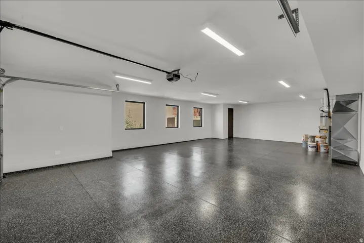 Spacious garage featuring a durable speckled epoxy floor, multiple windows, ample overhead lighting, and built-in shelving