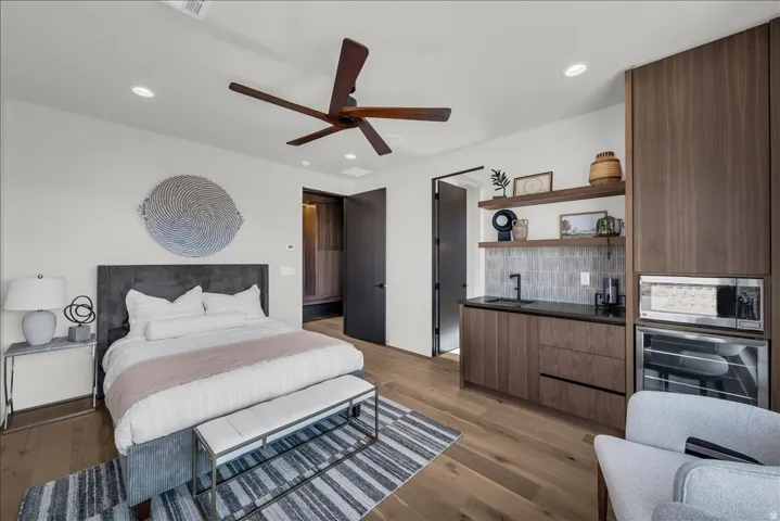 Hardwood flooring throughout, a modern ceiling fan, recessed lighting, built-in cabinetry with integrated appliances, and a wet bar with a tiled backsplash