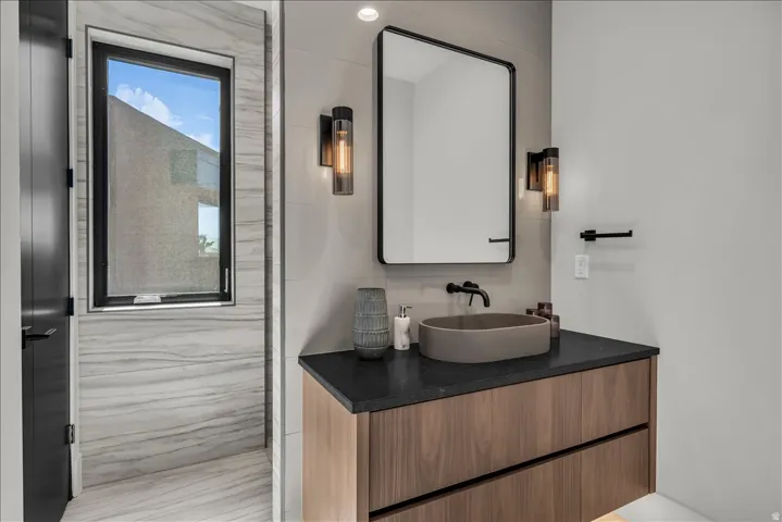 Floating wood-finish vanity with a vessel sink, dark countertop, and matte black faucet