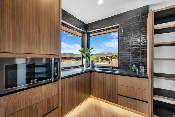 Built-in stainless steel microwave, wood-finish cabinetry, dark stone countertops, black subway tile backsplash, and integrated shelving
