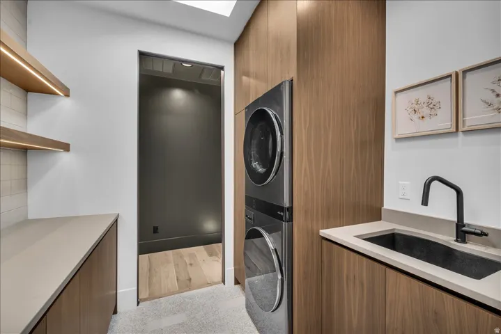 Wood-finish cabinetry, light-toned countertops, built-in stacked appliances, and a dark undermount sink with a matte black faucet