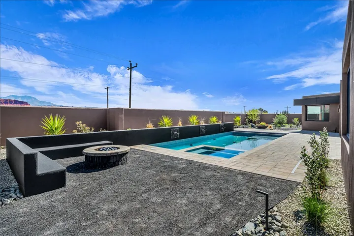 Backyard oasis featuring a swimming pool, integrated spa, adjacent paved patio, and a built-in fire pit with a surrounding bench