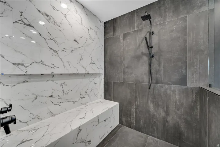 Spacious walk-in shower with large format white and gray marble-look wall tiles, built-in bench, recessed shelf, and matte black shower fixtures