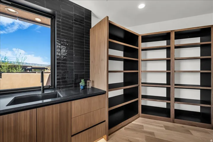 Window with black framing, black subway tile backsplash, integrated sink with matte black faucet, wood-finish cabinetry with drawers, and built-in shelving