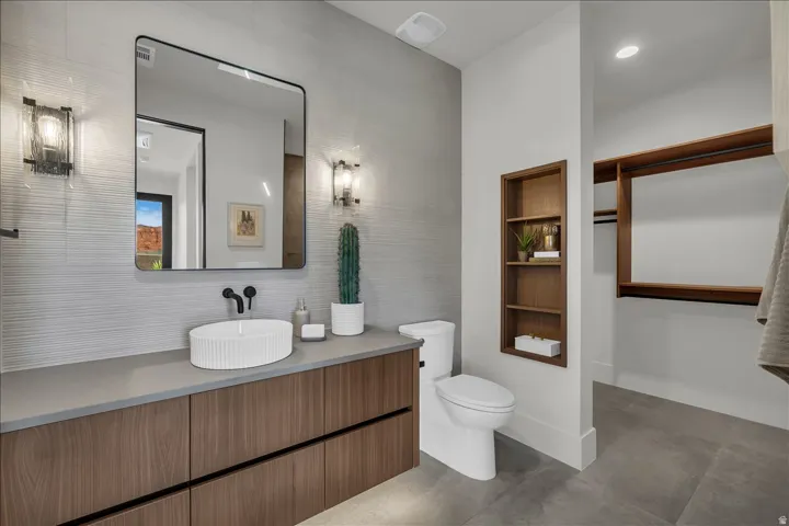 Wood-finish vanity with a vessel sink, dark fixtures, and textured wall tile