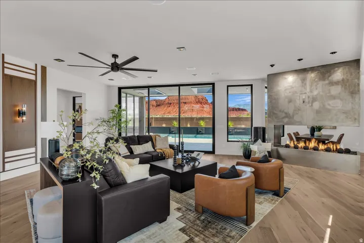 Expansive living area featuring light wood-finish flooring, a contemporary ceiling fan, and a built-in linear fireplace with a textured surround