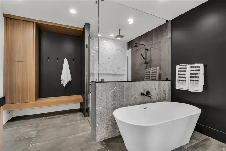 Freestanding soaking tub, walk-in glass shower, built-in bench, wood-finish cabinetry, and large format floor tiling