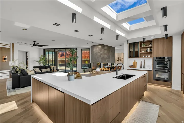 Expansive kitchen island with a white countertop and integrated sink, wood-finish cabinetry, built-in double ovens, and multiple skylights