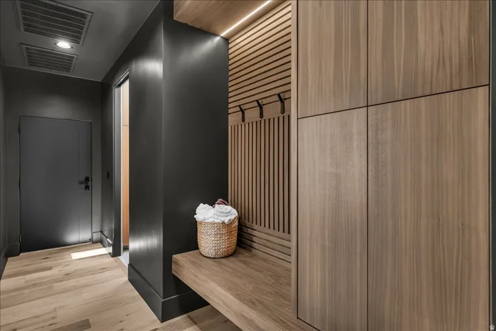 Built-in wood-finish cabinetry, integrated bench seating, accent slat wall with coat hooks, and recessed ceiling lighting