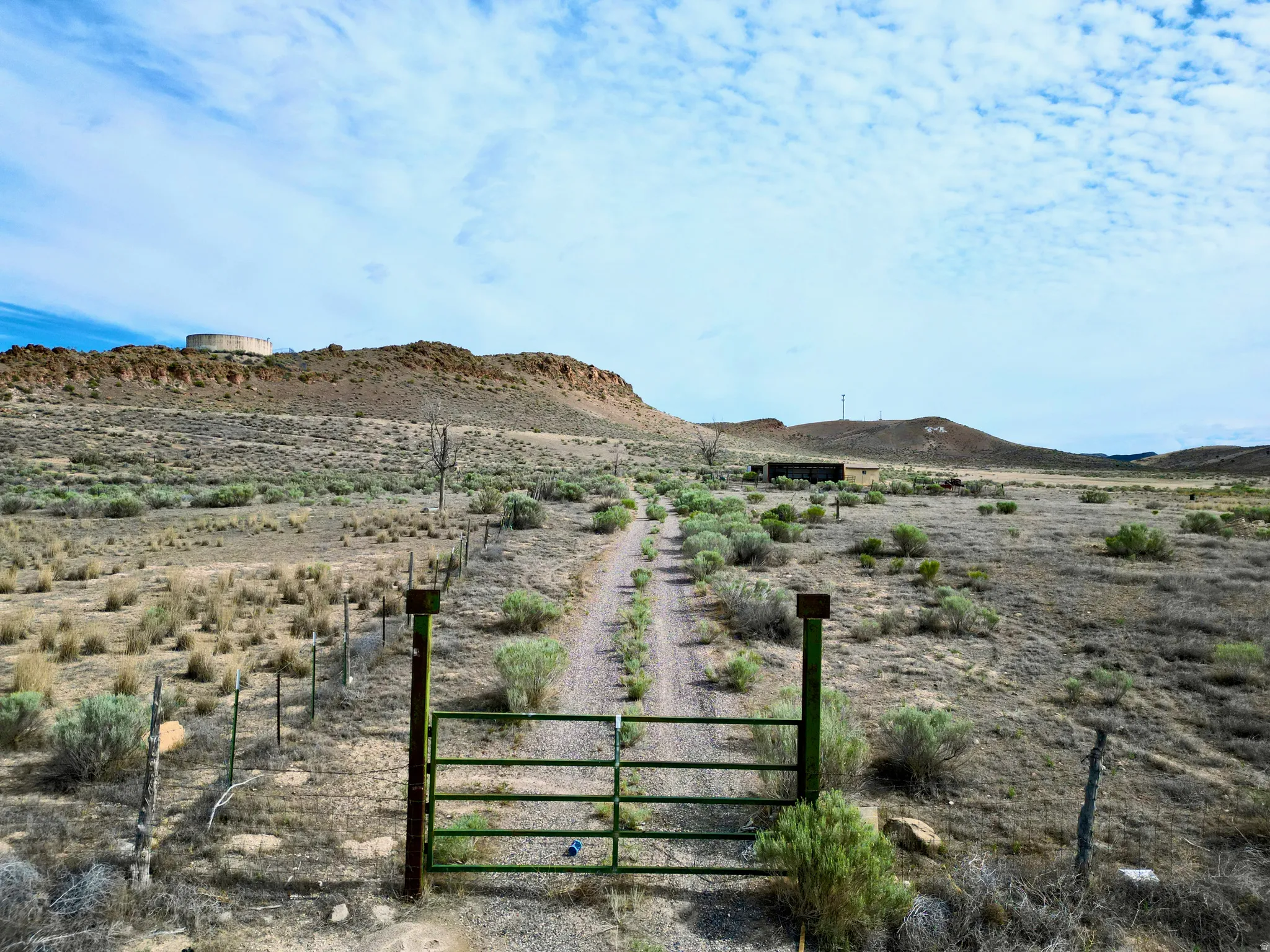 Gated property entrance with a dirt road, surrounded by desert vegetation and fencing