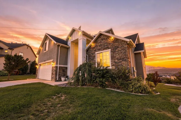 Contemporary architecture featuring a stone and stucco exterior, prominent gables, an attached garage, and mature landscaping