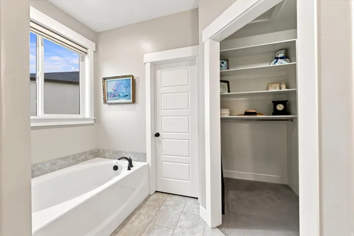 Soaking tub with a matte black faucet, a large window, and light-toned wall tile