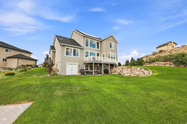 Expansive rear yard with a manicured lawn, tiered landscaping with natural rock elements, and a multi-level stucco exterior
