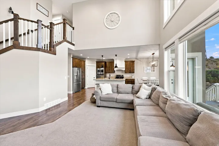 Two-story ceiling, large windows, wood-finish flooring, staircase with wood and white balusters, and a kitchen with wood cabinetry
