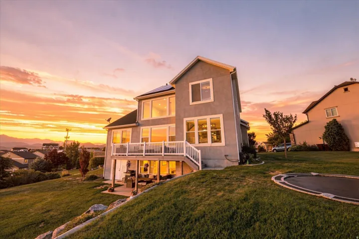 Stucco exterior with multiple windows, upper-level balcony, lower-level patio, and a sloped backyard