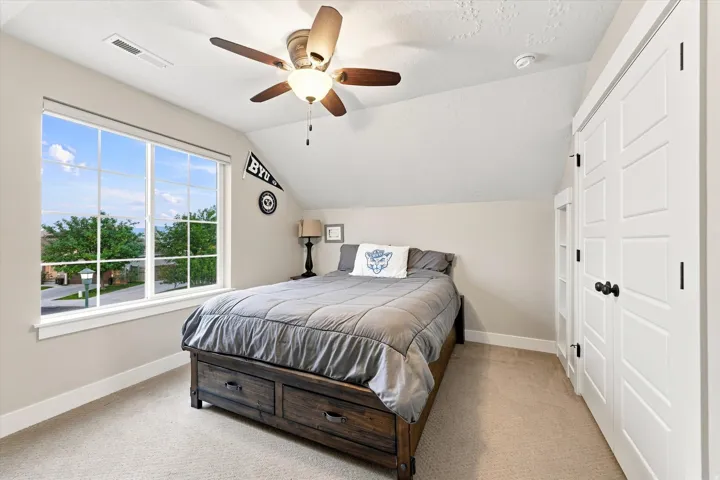 Angled ceiling bedroom featuring a ceiling fan with integrated lighting, a large multi-pane window, and white panel doors