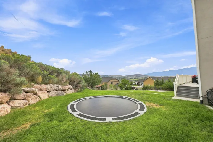 Expansive backyard featuring a manicured lawn, stone retaining wall, terraced landscaping, and a built-in trampoline