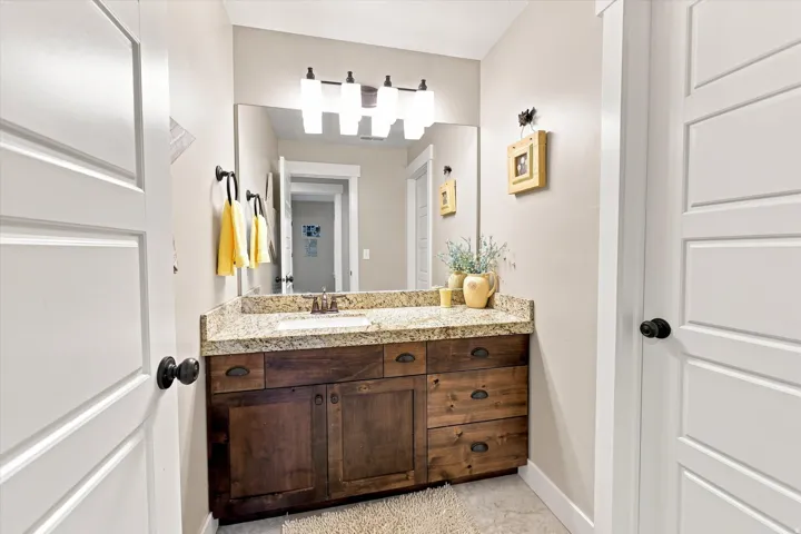 Wood-finish vanity with a light-toned countertop, undermount sink, and wall-mounted light fixture