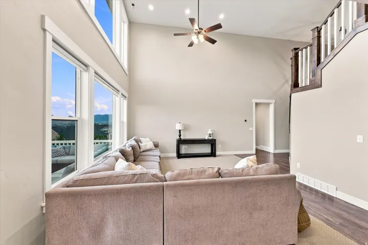 Soaring ceilings with recessed lighting, expansive windows, a ceiling fan, wood-finish flooring, and a staircase with wood railings
