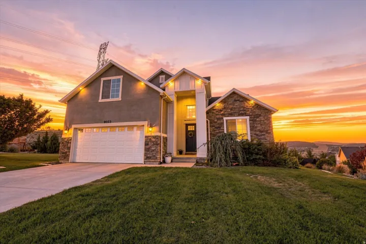 Stucco and stone exterior with architectural gables, front-facing garage, and established landscaping