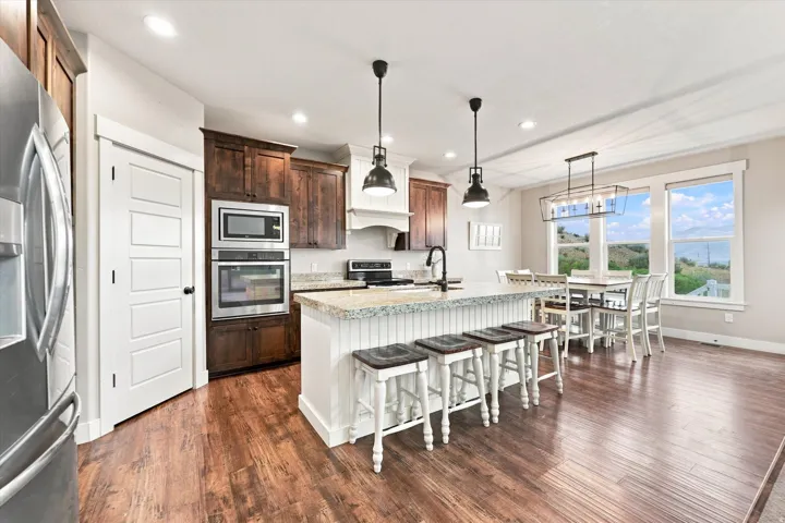 Kitchen featuring wood-finish flooring, dark wood cabinetry, a center island with counter seating, stainless steel appliances, and multiple windows