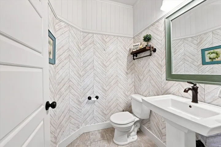 Pedestal sink with dark bronze faucet, framed mirror, and chevron pattern wall paneling