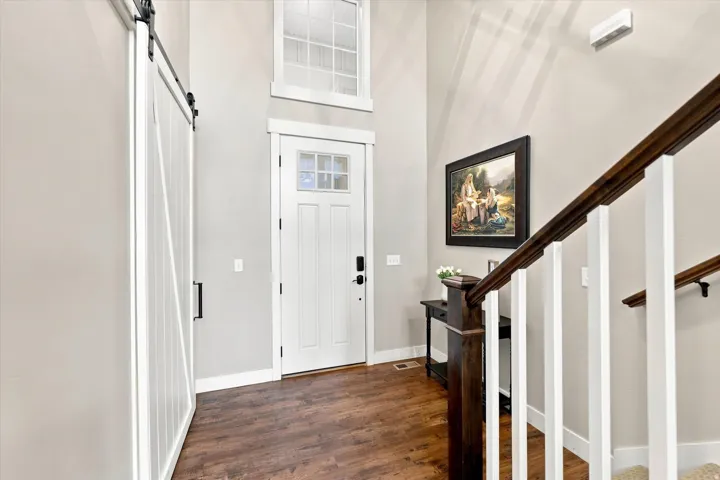 Entryway featuring a white barn door, wood-finish flooring, a white paneled entry door with frosted glass, and a staircase with dark wood handrails and white balusters