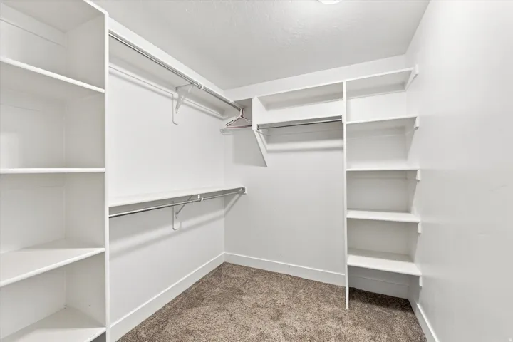 Walk-in closet featuring built-in shelving, multiple hanging rods, and carpet flooring