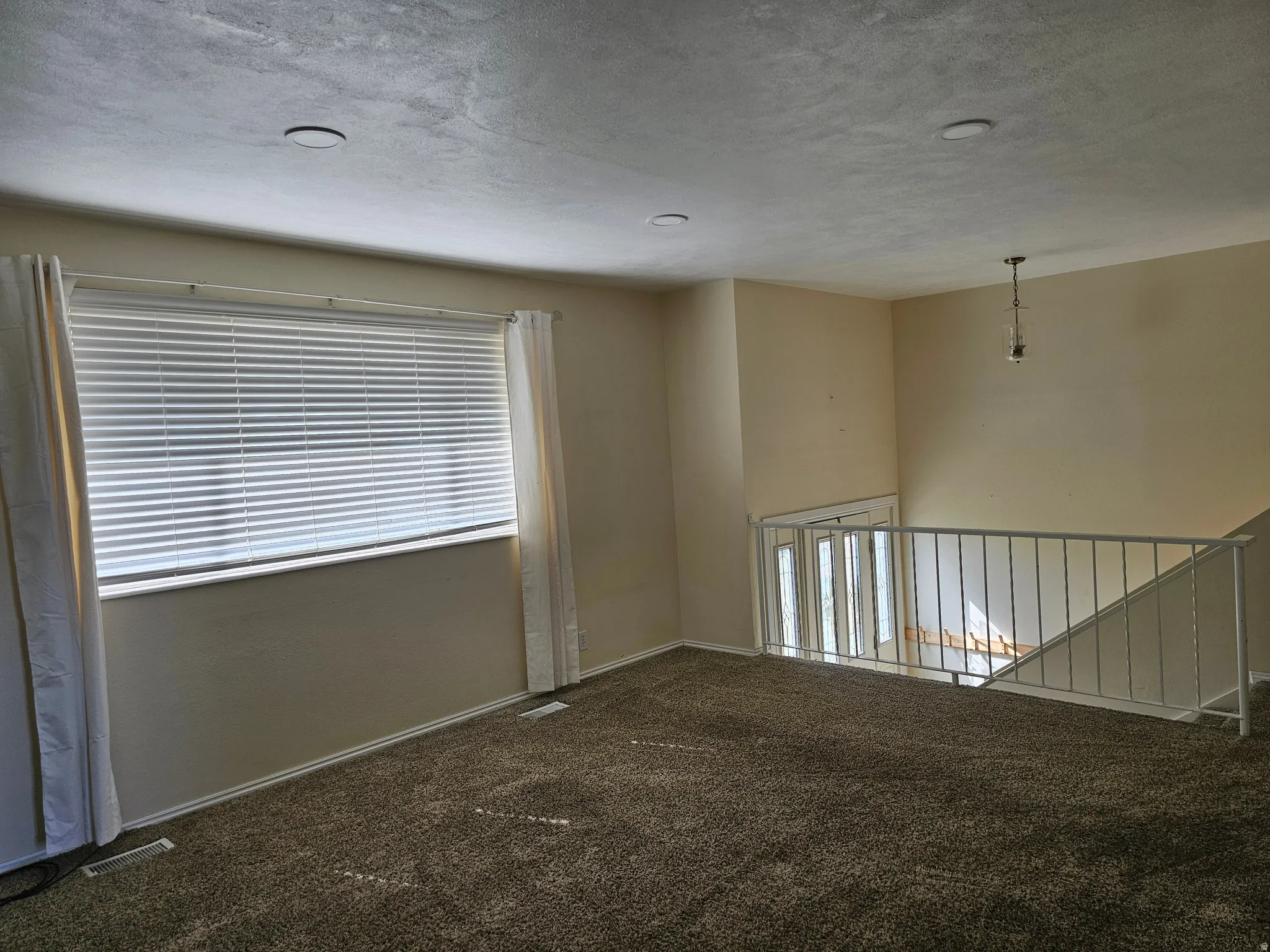 Carpeted upper level with recessed lighting, a large window, and a metal railing overlooking the lower level